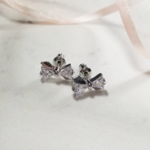 Boucles d'oreilles en forme de nœud papillon, composées de deux pierres de zircon en forme de triangle, petites et délicates. Bow-shaped earrings made with two triangular zircon stones, small and delicate.